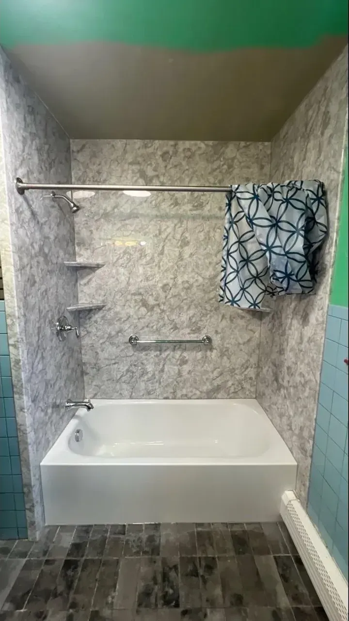 A white bathtub with grey marbled wall panels, a shower curtain, and a grab bar in a bathroom with teal tiled walls.