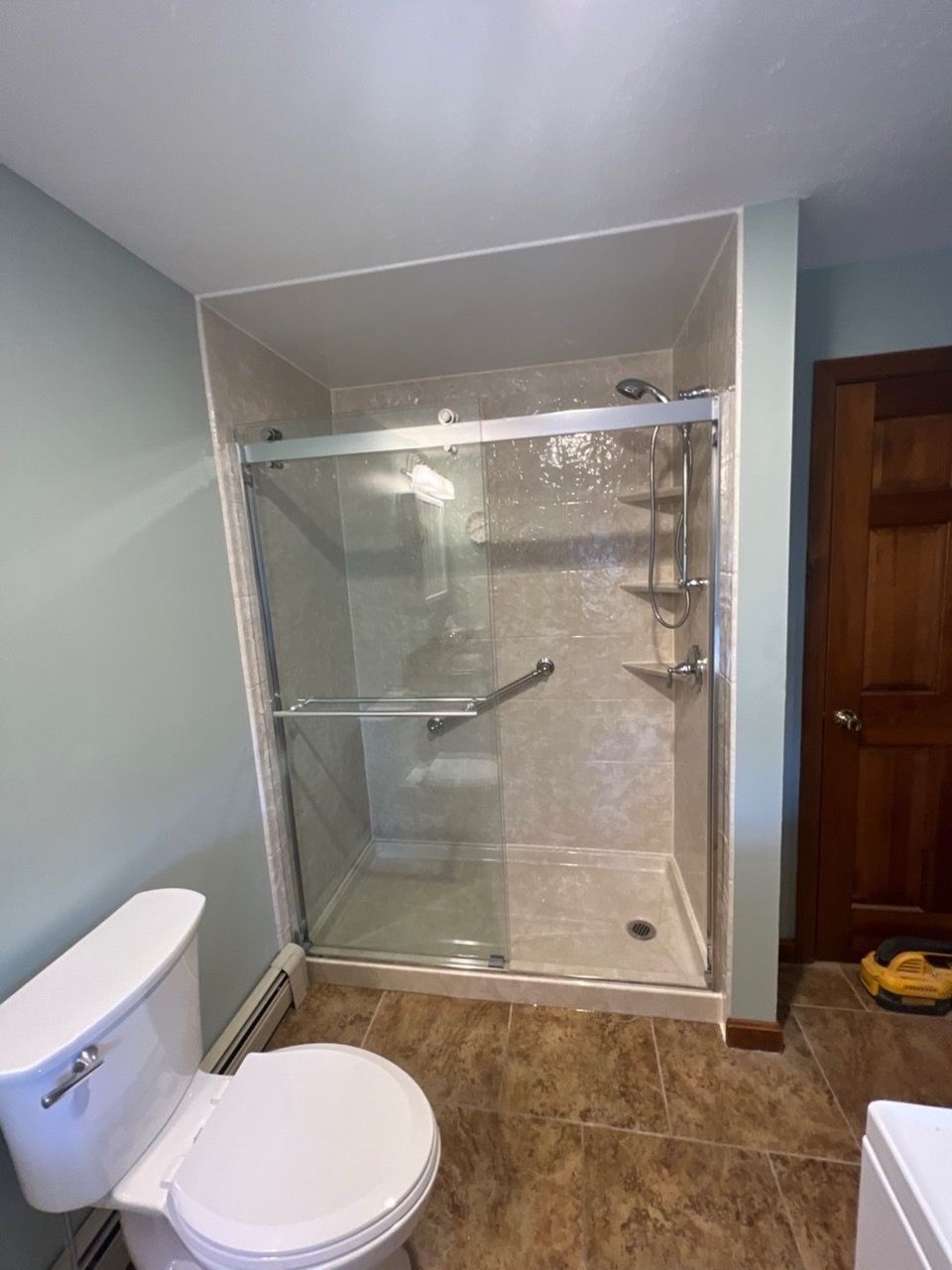 A bathroom featuring a glass-enclosed walk-in shower with light-colored tile walls, a toilet, and brown patterned flooring.