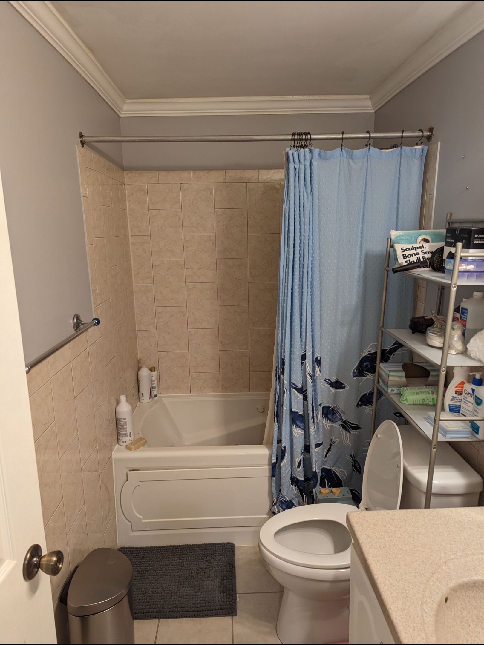 A small, neutral-toned bathroom featuring a bathtub with tan tile walls, a blue shower curtain, and a toilet.