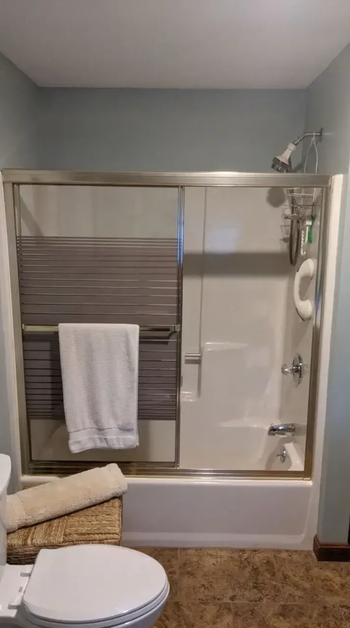 A bathroom with a sliding glass shower door and white tub, featuring a white towel hanging over the frame.