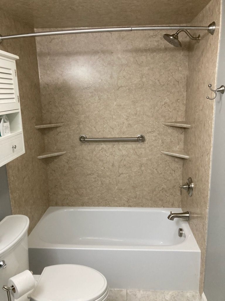 A tan, speckled-pattern shower and bathtub unit with a metal grab bar, shelves, and a showerhead, next to a white toilet.