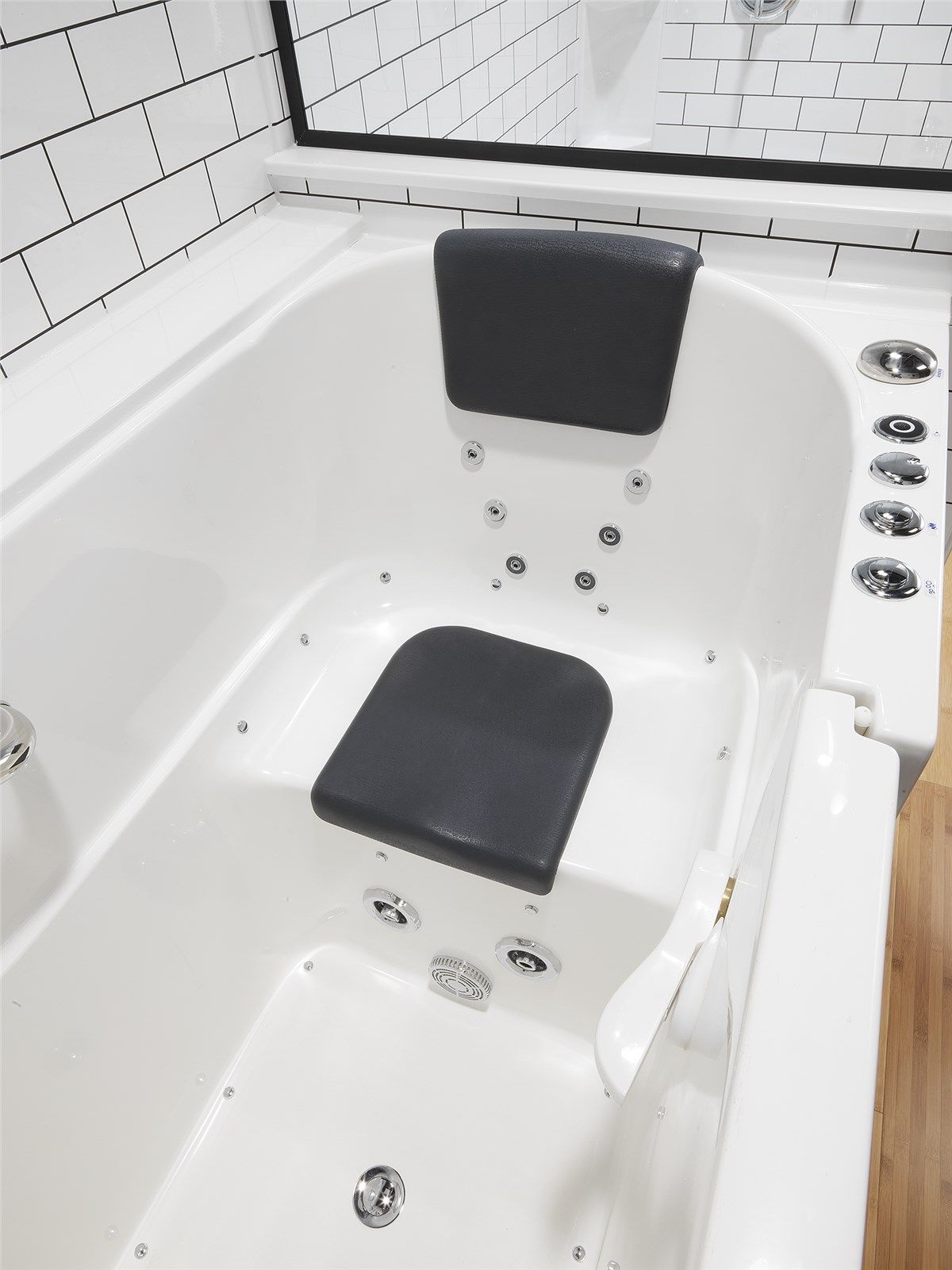 White walk-in bathtub with a dark seat and headrest, chrome hydrotherapy jets, and white subway tile wall background.