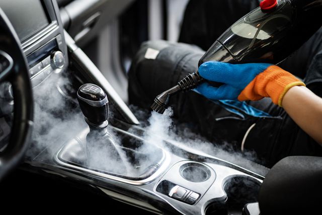 Gloved hand cleaning a car’s center console with a cloth and spray cleaner