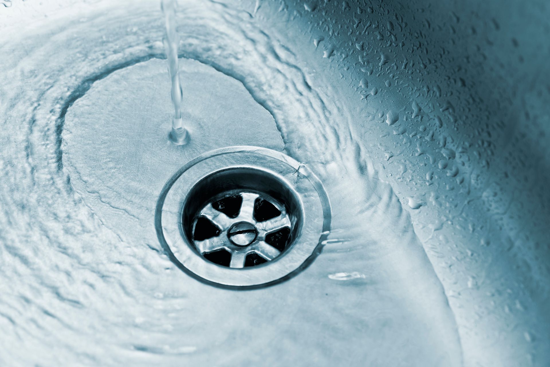 Close-up of a metal sink drain with water swirling around it