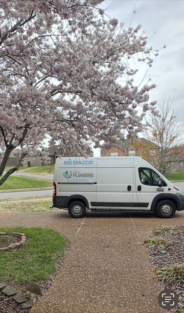 White service van parked on a gravel driveway under blooming pink trees in a residential yard