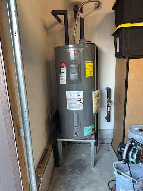 Water heater in a narrow utility closet with pipes, warning labels, and a bucket on the floor