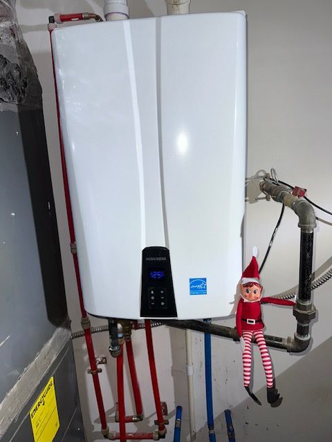 Wall-mounted white boiler with pipes and a small elf doll hanging on the right side.
