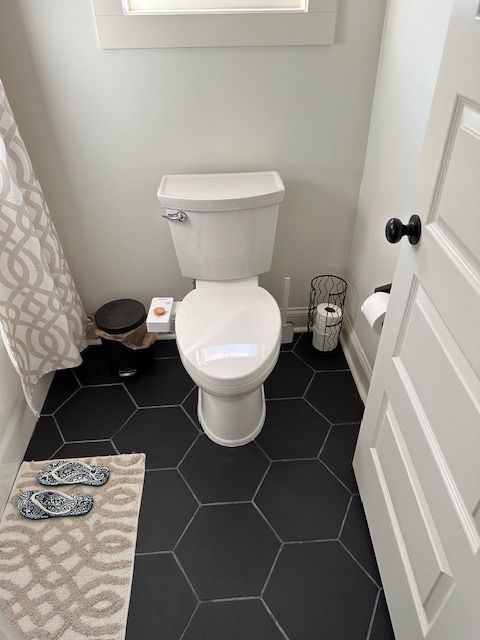 Small bathroom with a white toilet, black hex tile floor, and patterned shower curtain.