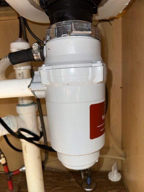 White under-sink garbage disposal with pipes and plumbing inside a cabinet