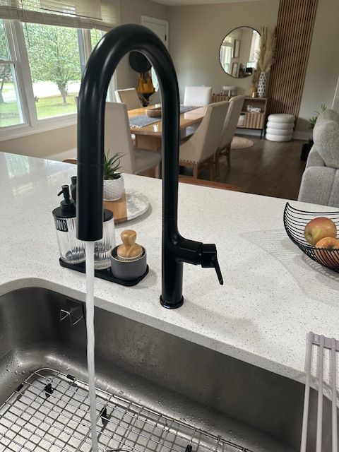 Black kitchen faucet over sink with running water, overlooking a bright dining area.
