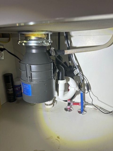 Under-sink garbage disposal and plumbing with a flashlight illuminating the cabinet floor