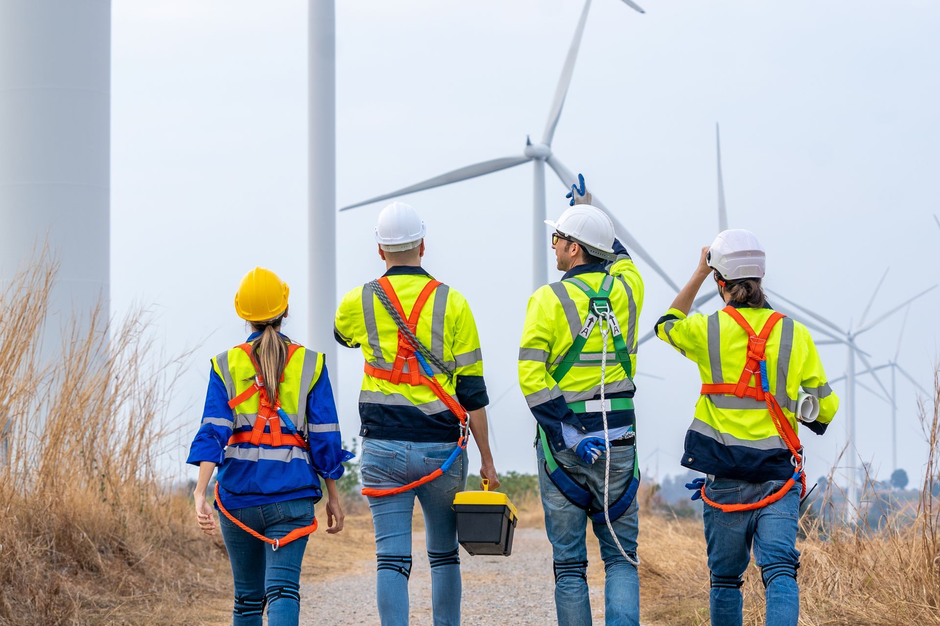 A group of construction workers are walking towards a wind turbine.