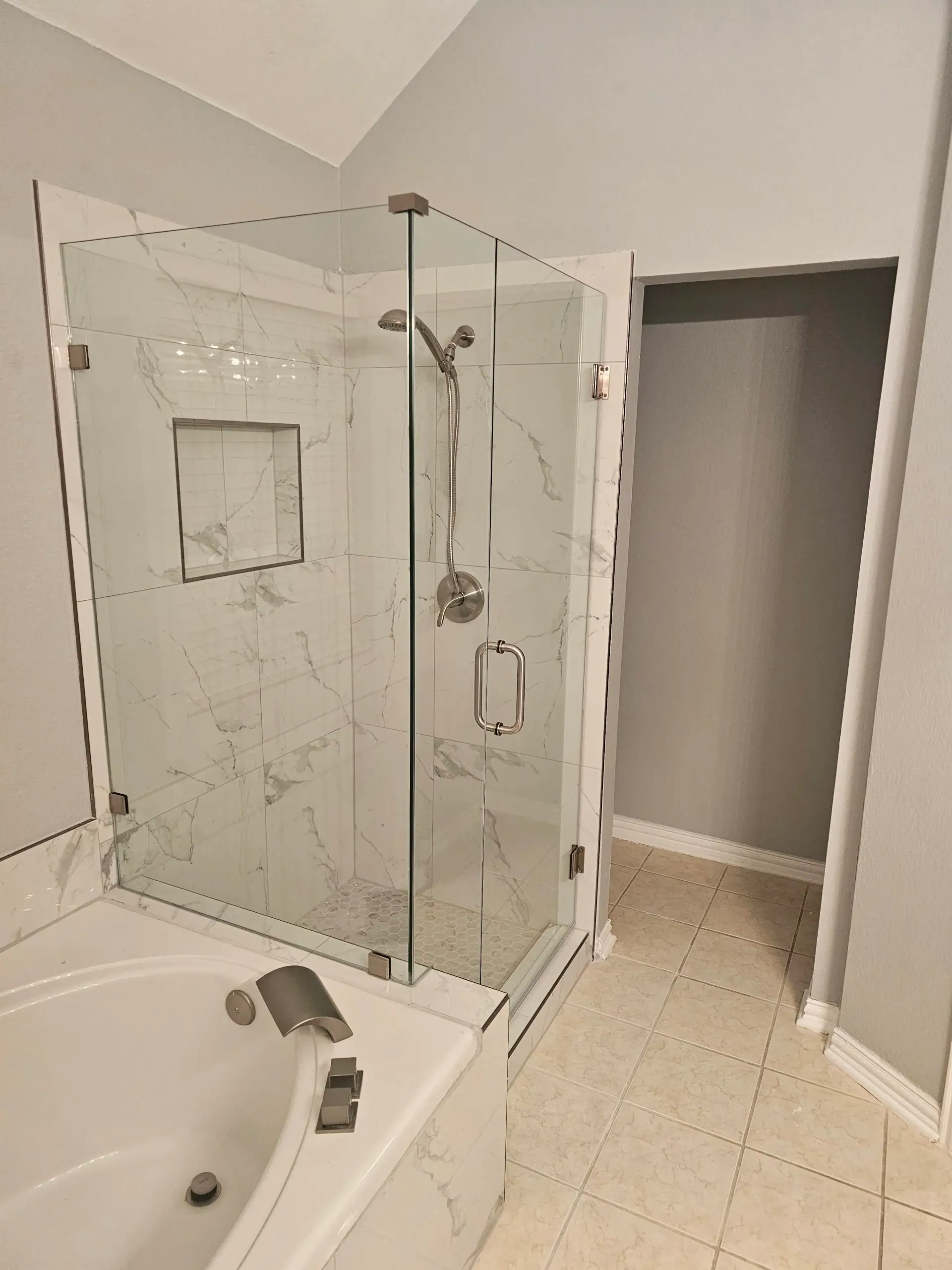 Bathroom with white tub and glass shower enclosure beside a gray-walled doorway.