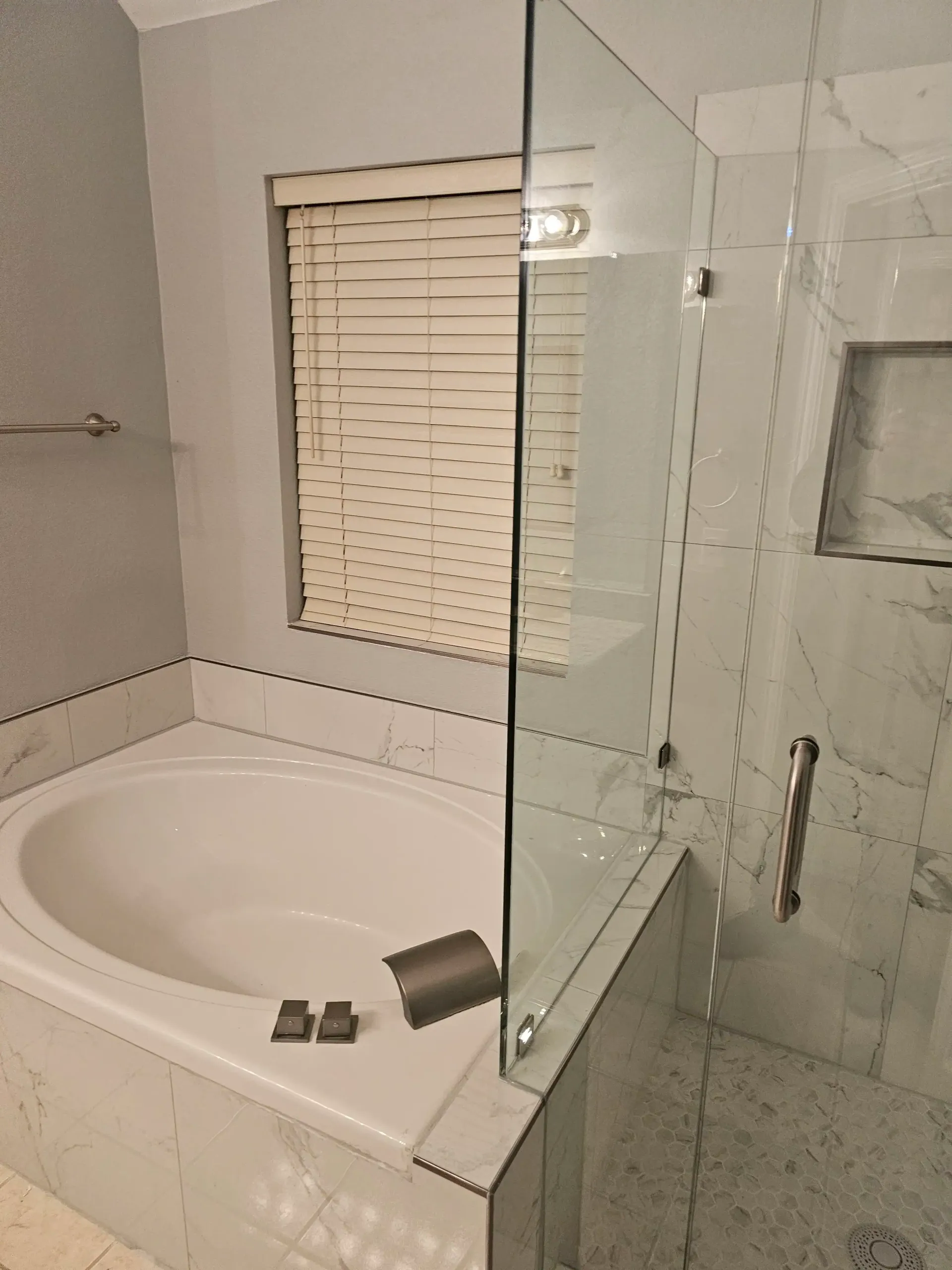 Bathroom with a white tub, shower with glass door, window with blinds.