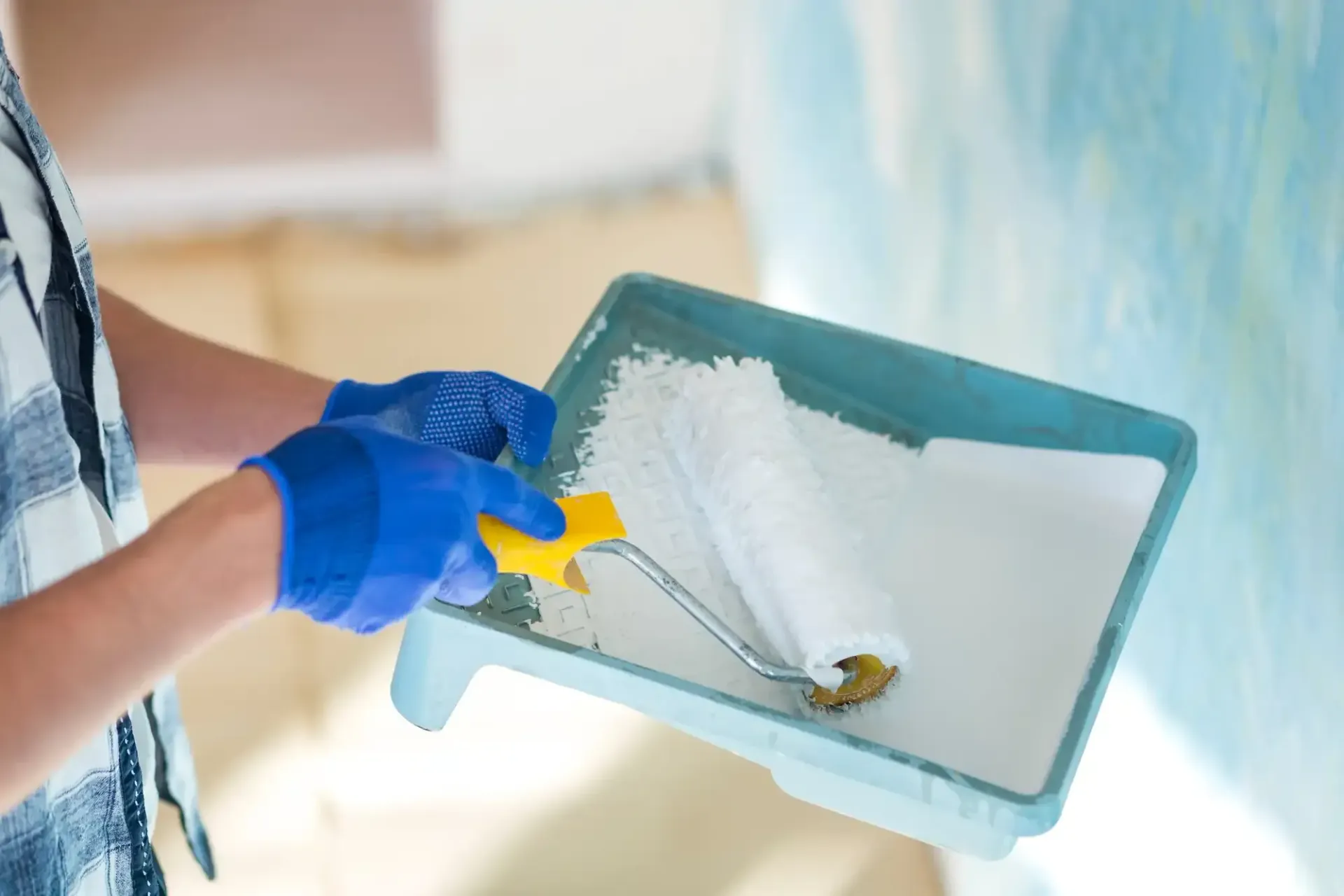 Gloved hand painting a wall corner with a roller and paint tray