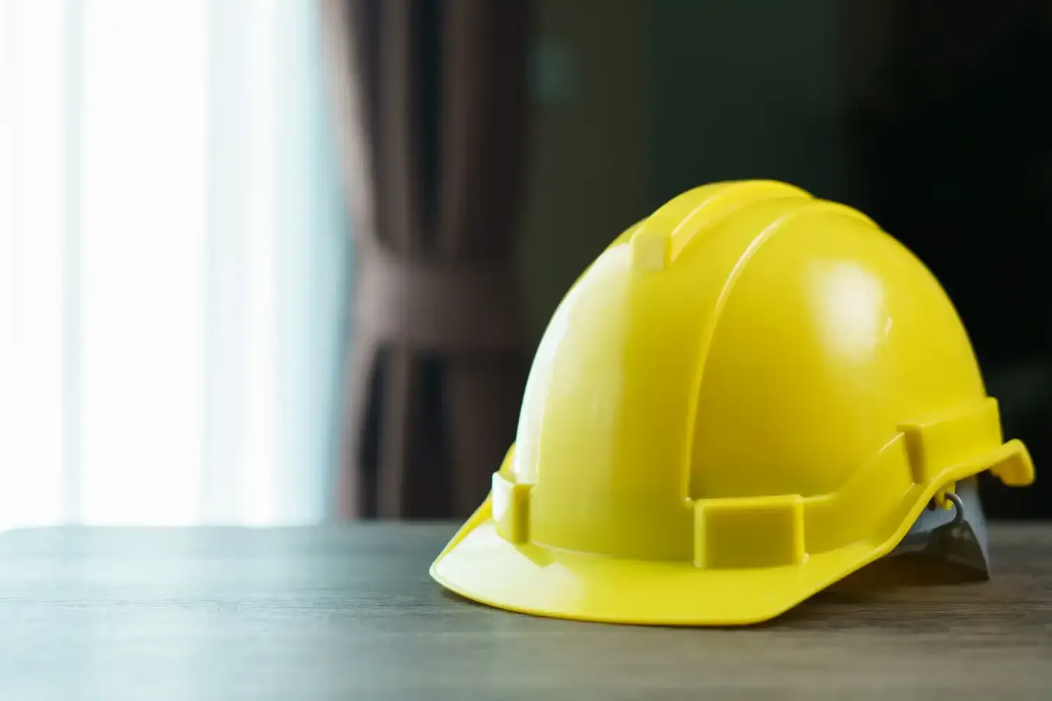 Yellow construction hard hat on a wooden surface near a window