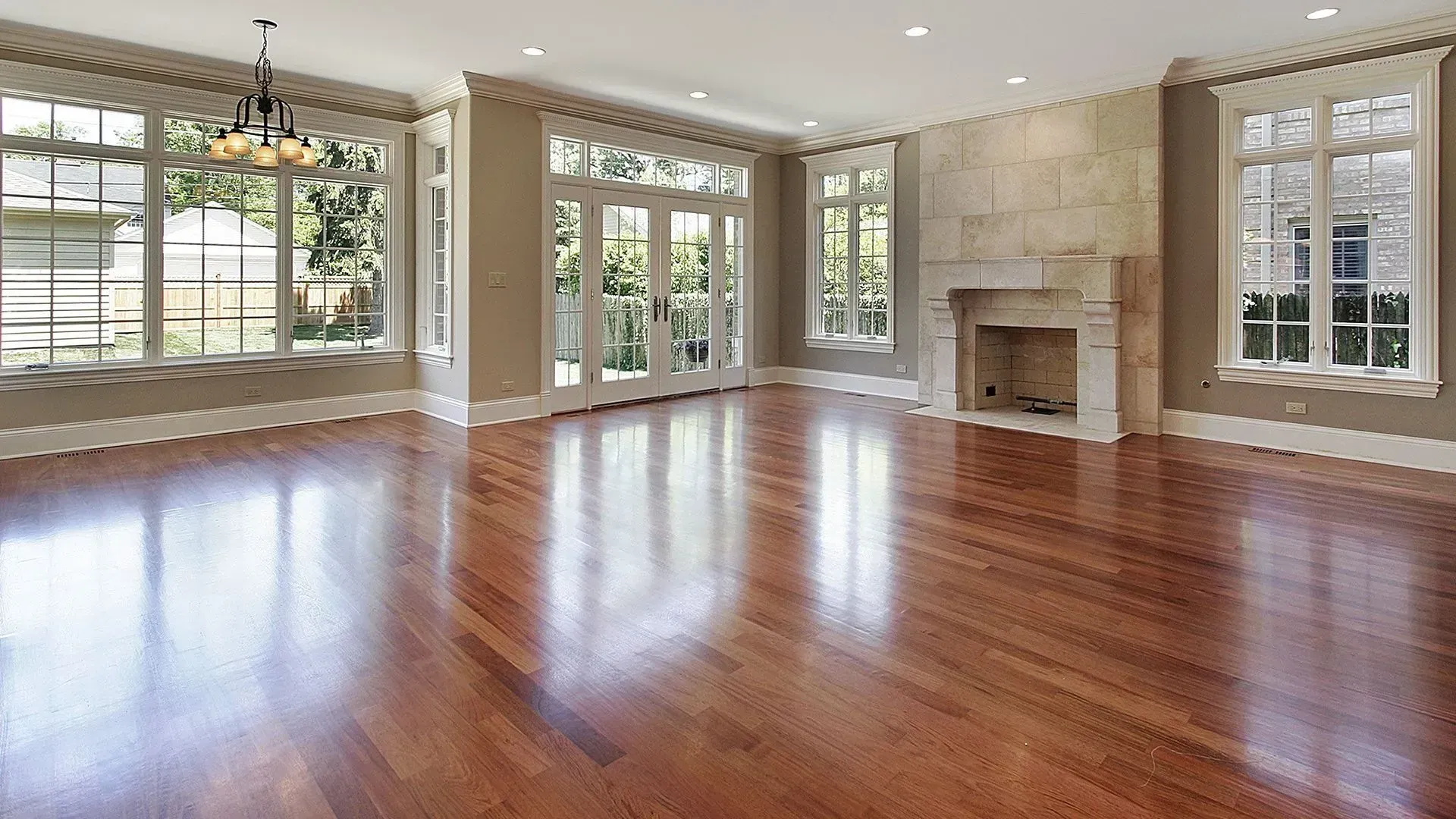 Empty room with hardwood floors, large windows, fireplace, and chandelier.