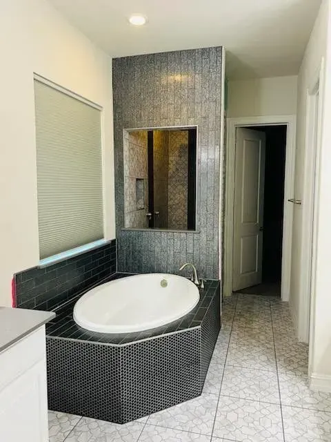 Bathroom with an oval bathtub enclosed in dark gray tile, accented by a tile wall feature.