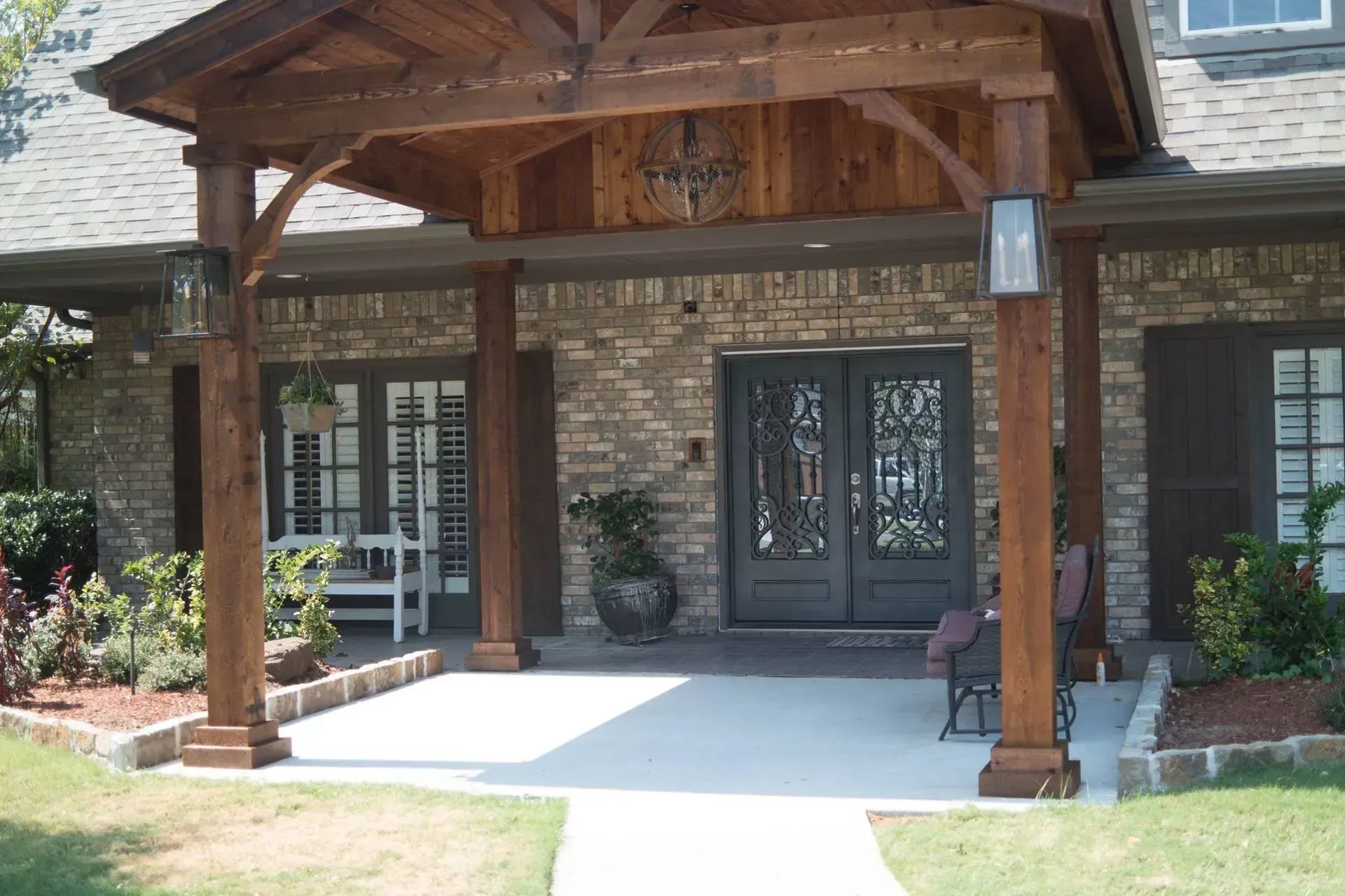 Brown wooden portico over a brick home's front door; two dark doors, lanterns, and concrete walkway.