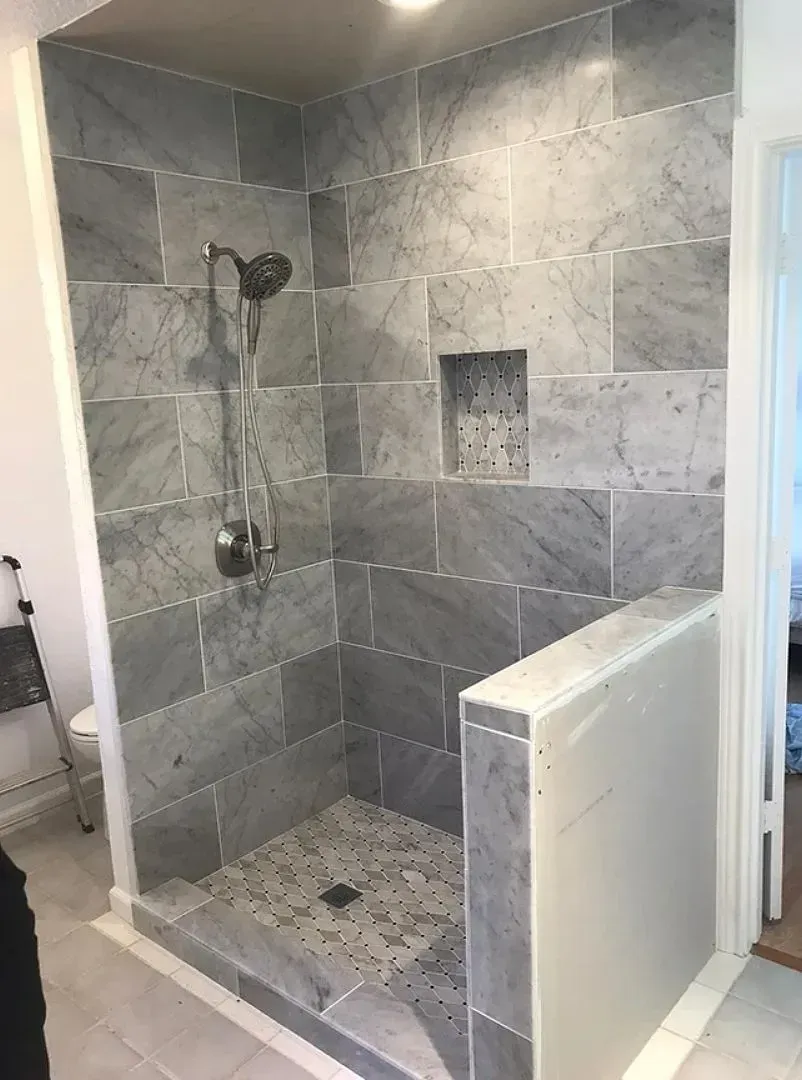 Gray tiled shower with a niche and shower head.