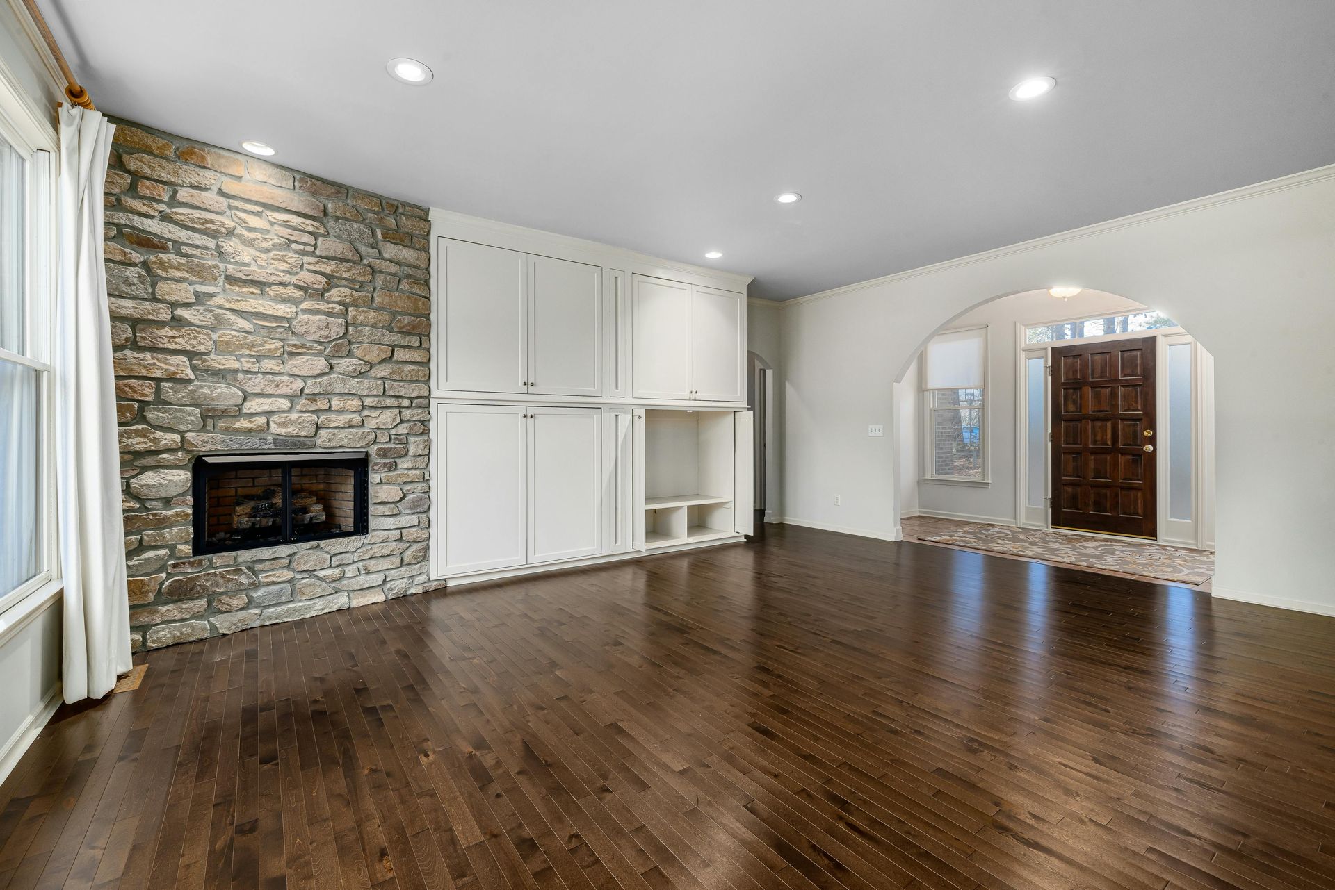 Living room with stone fireplace, white cabinets, and dark hardwood floors.