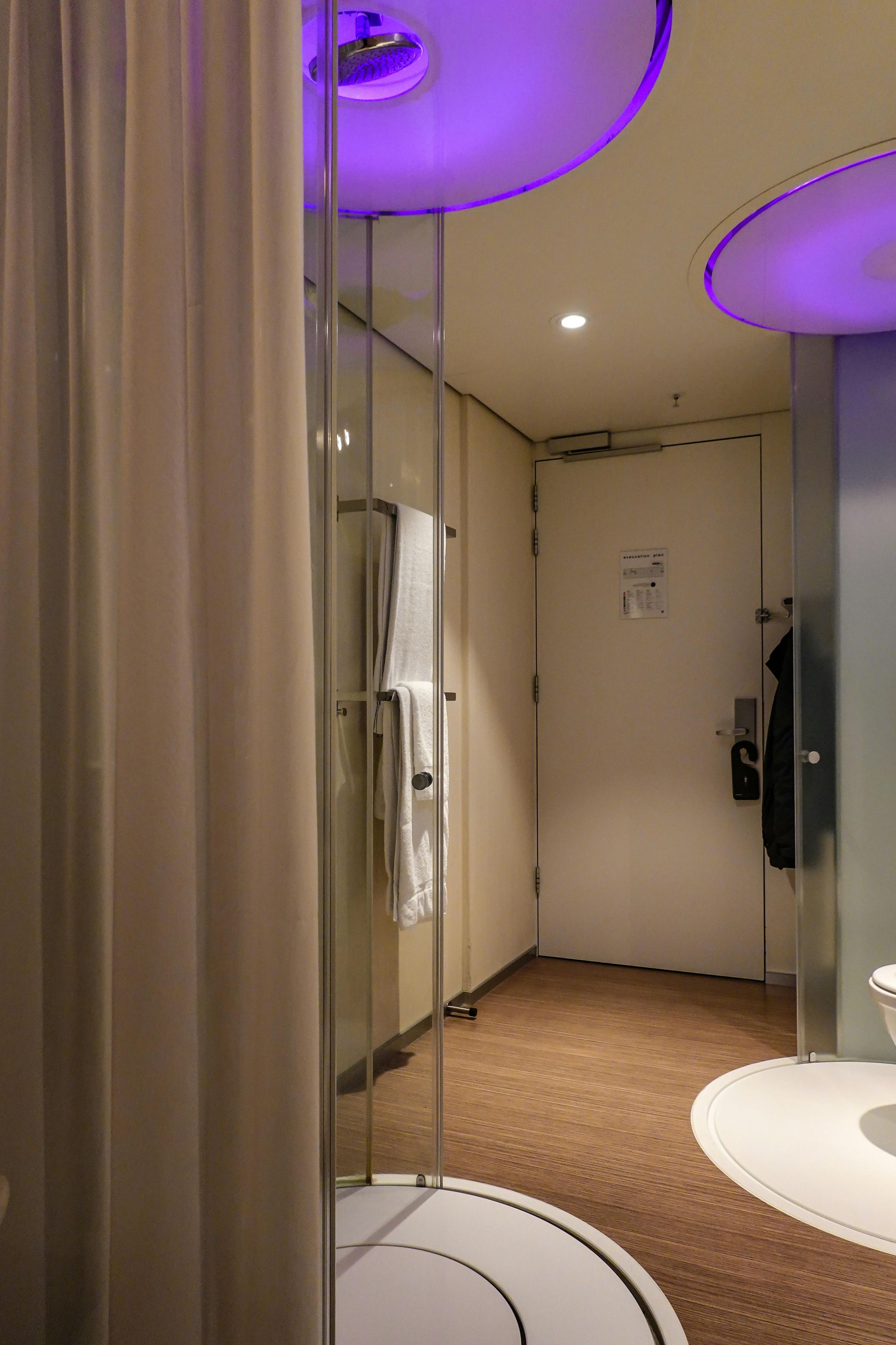 Modern bathroom interior with glass shower, white fixtures, and purple ceiling lights