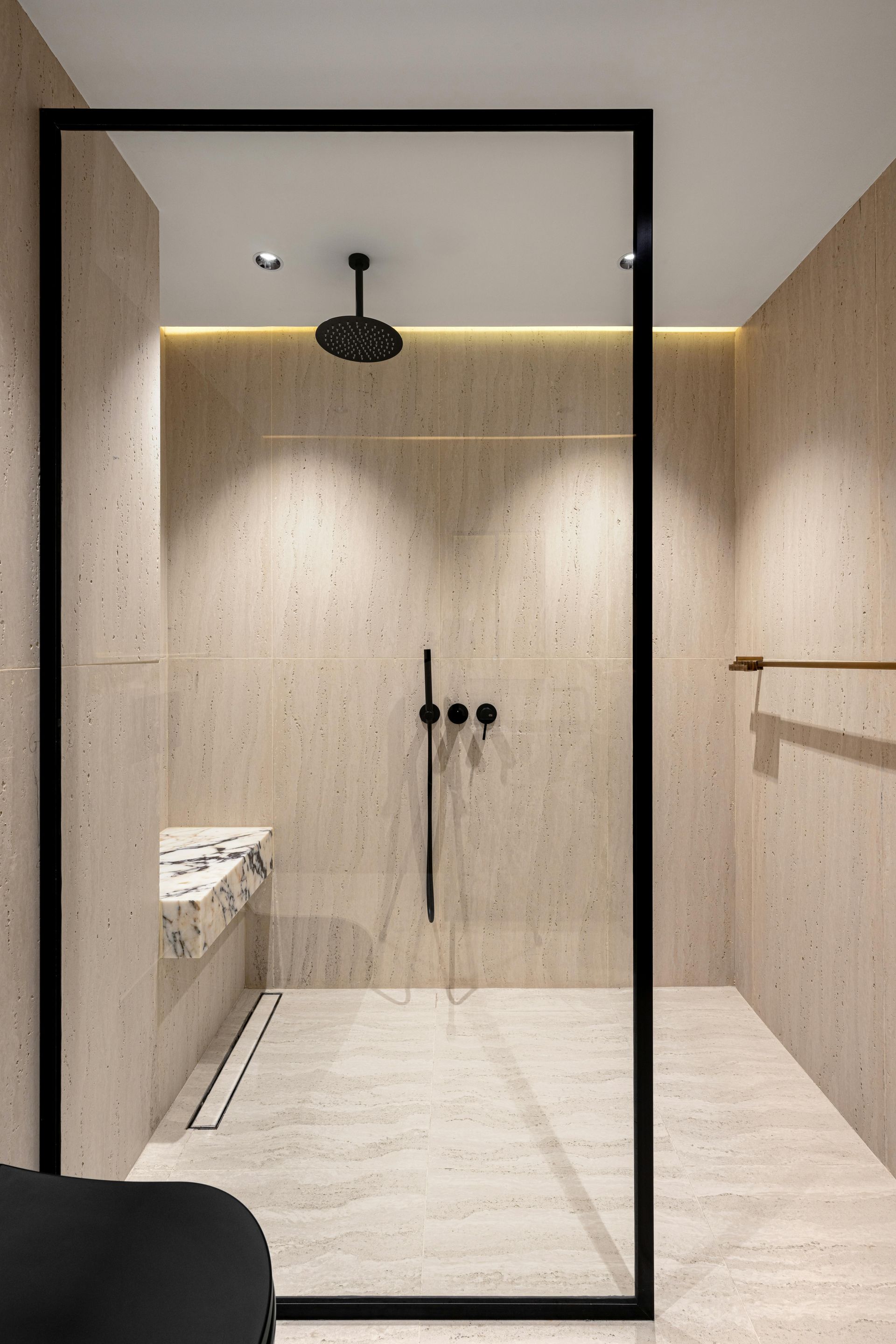 Modern minimalist bathroom with glass shower, beige tile walls, black fixtures, and a marble sink counter