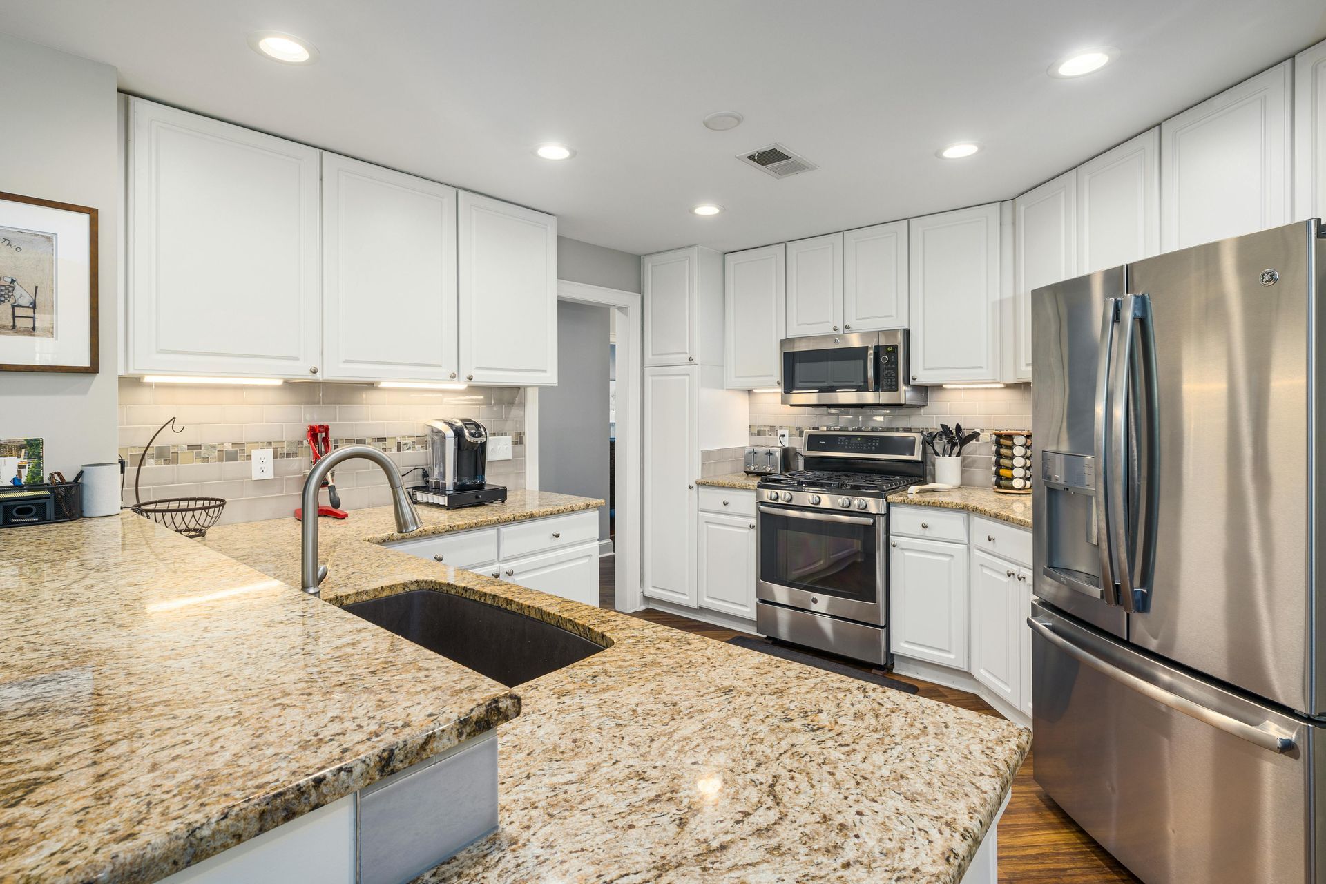 Bright modern kitchen with white cabinets, granite countertops, stainless steel appliances, and recessed lighting