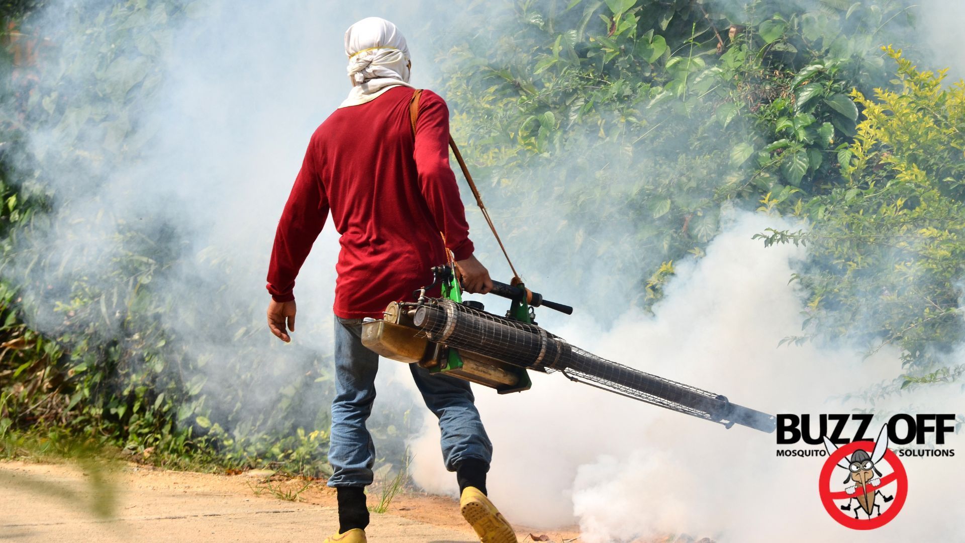 A man is walking down a dirt road holding a machine that is spraying smoke.