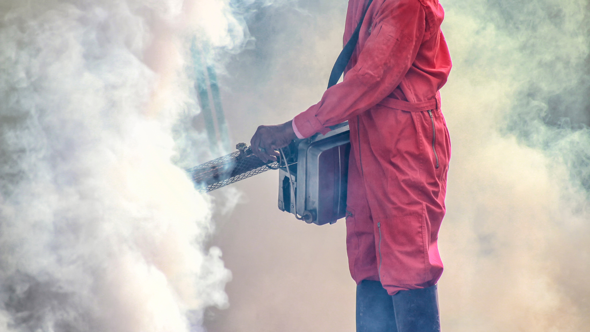 A man in a red jumpsuit is holding a machine that is spraying smoke.