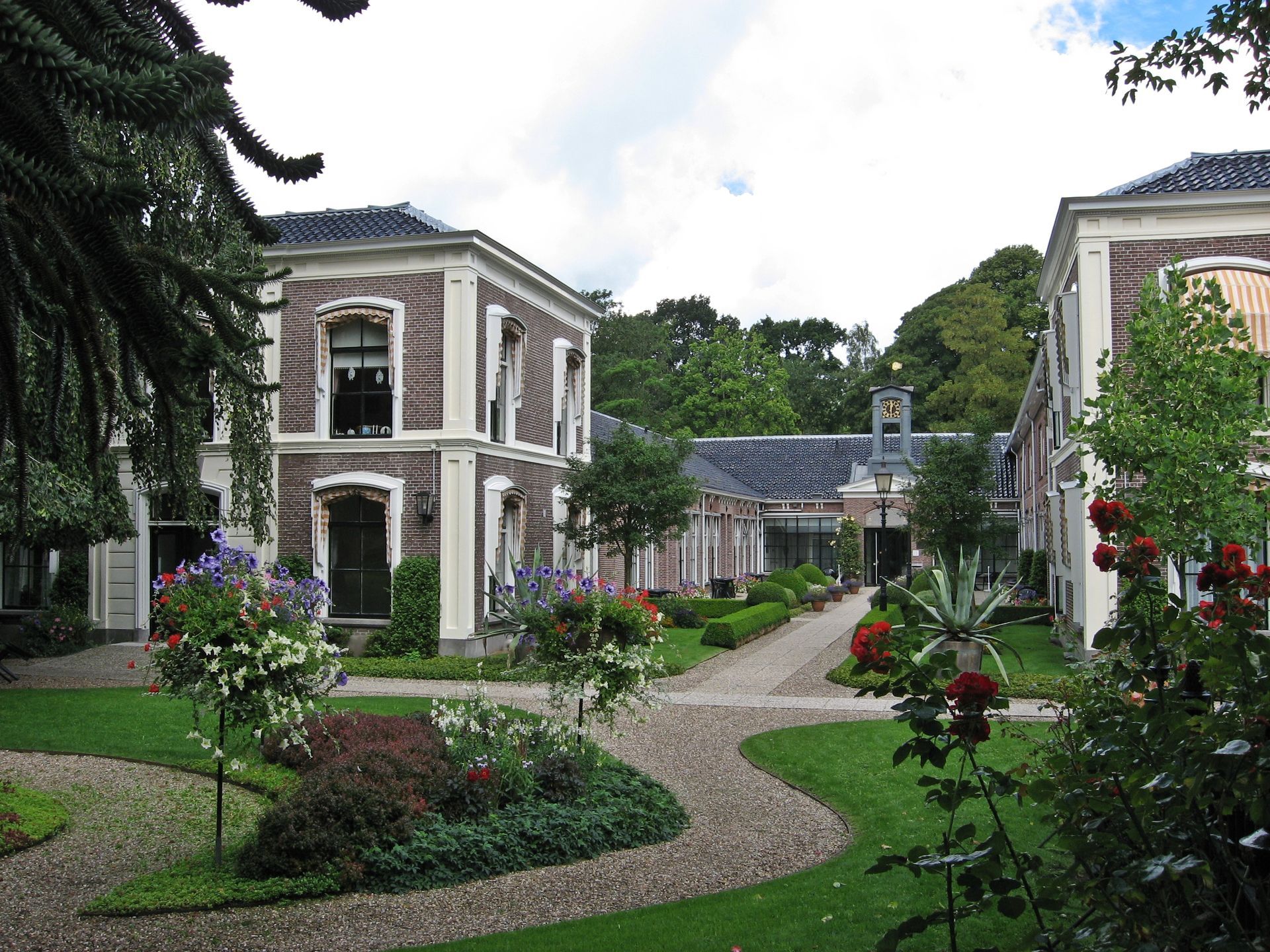 Een elegante tuin met een kronkelend stenen pad tussen witte gebouwen en bloeiende bloemperken.