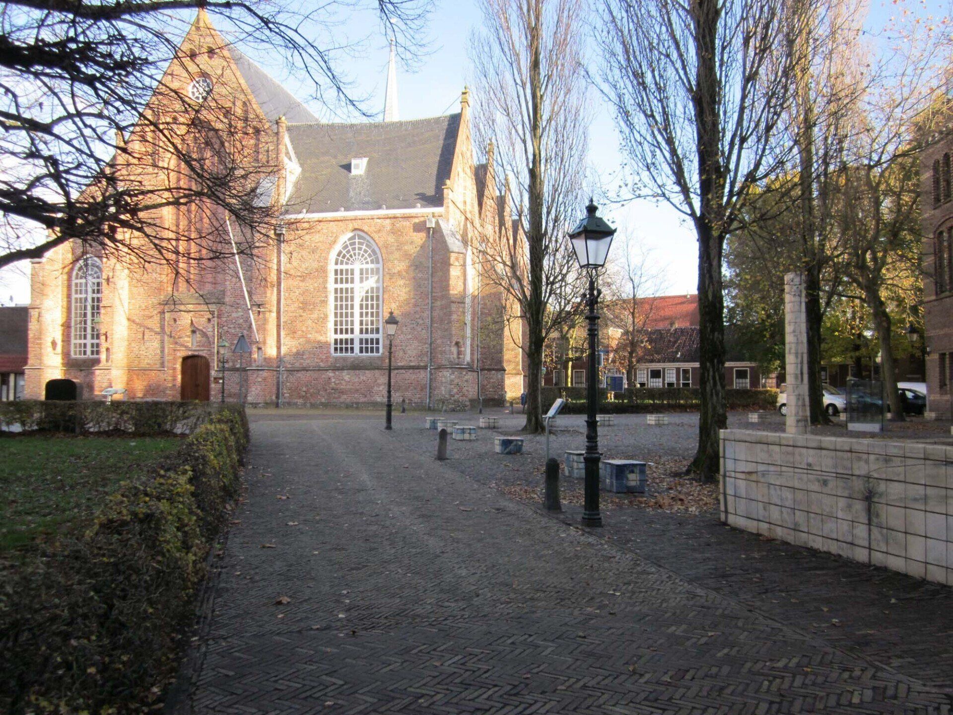 Historische bakstenen kerk aan een geplaveid pad, met bomen, lantaarnpalen en een rustige binnenplaats.