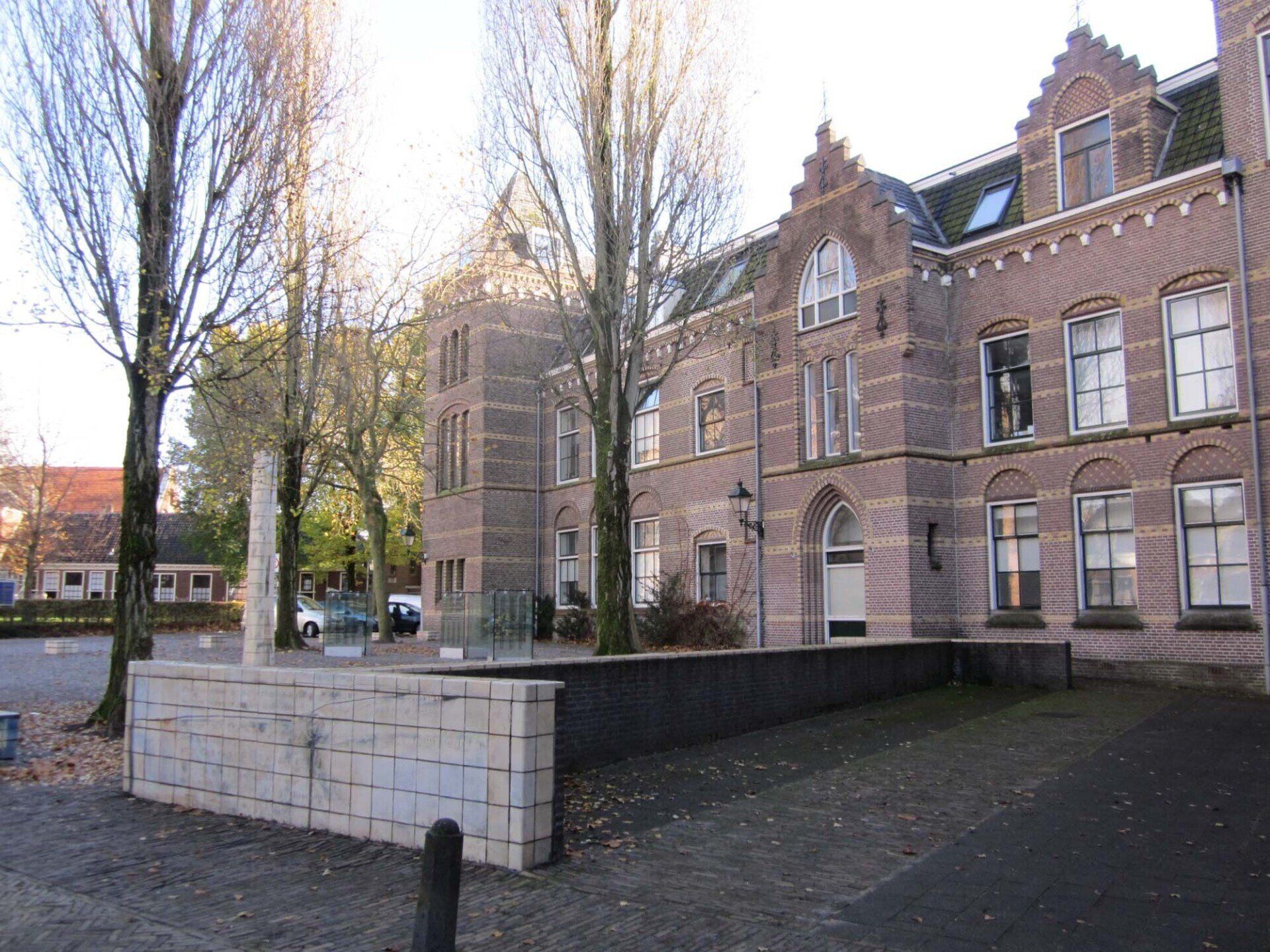 Een bakstenen schoolgebouw met boogvensters en een kleine binnenplaats omzoomd door hoge bomen.