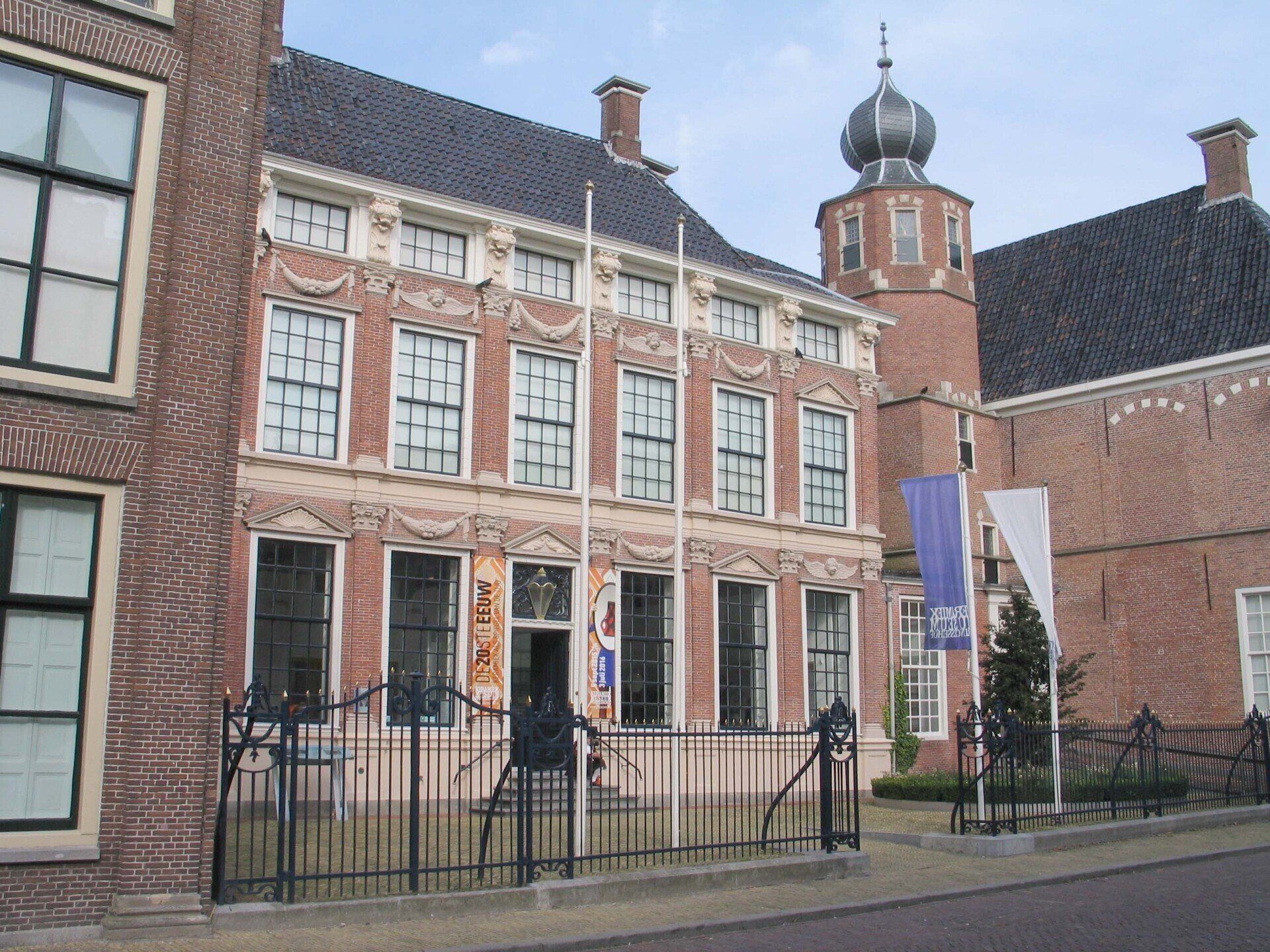 Historisch bakstenen gebouw met wit omlijste ramen en een kleine zwarte koepeltoren achter een smeedijzeren hek.