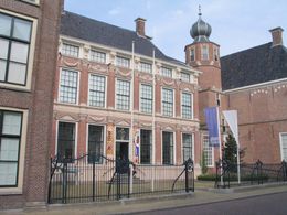 Historisch bakstenen gebouw met wit omlijste ramen en een kleine zwarte koepeltoren achter een smeedijzeren hek.