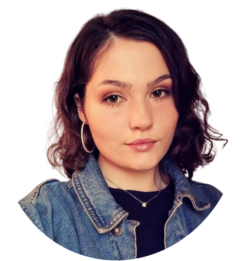 Woman with brown hair and hoop earrings, wearing a denim jacket and necklace, looking at the camera.