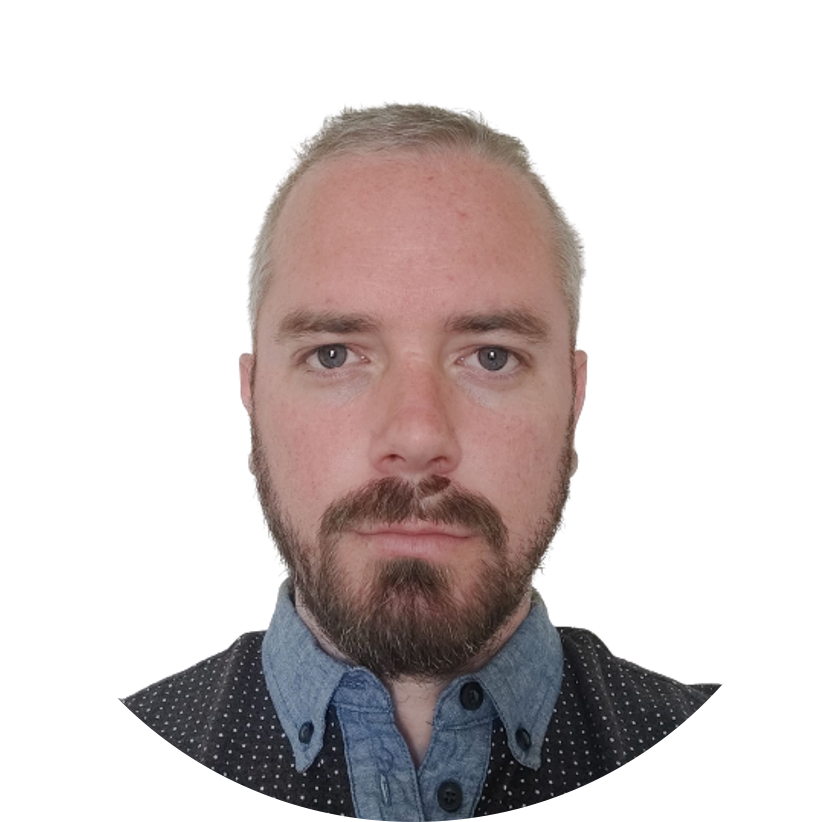 Man with a beard and light hair wearing a blue denim shirt and a dark shirt.