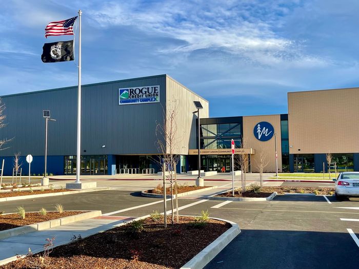Modern commercial building with a blue facade, U.S. and POW/MIA flags, and parking lot in front