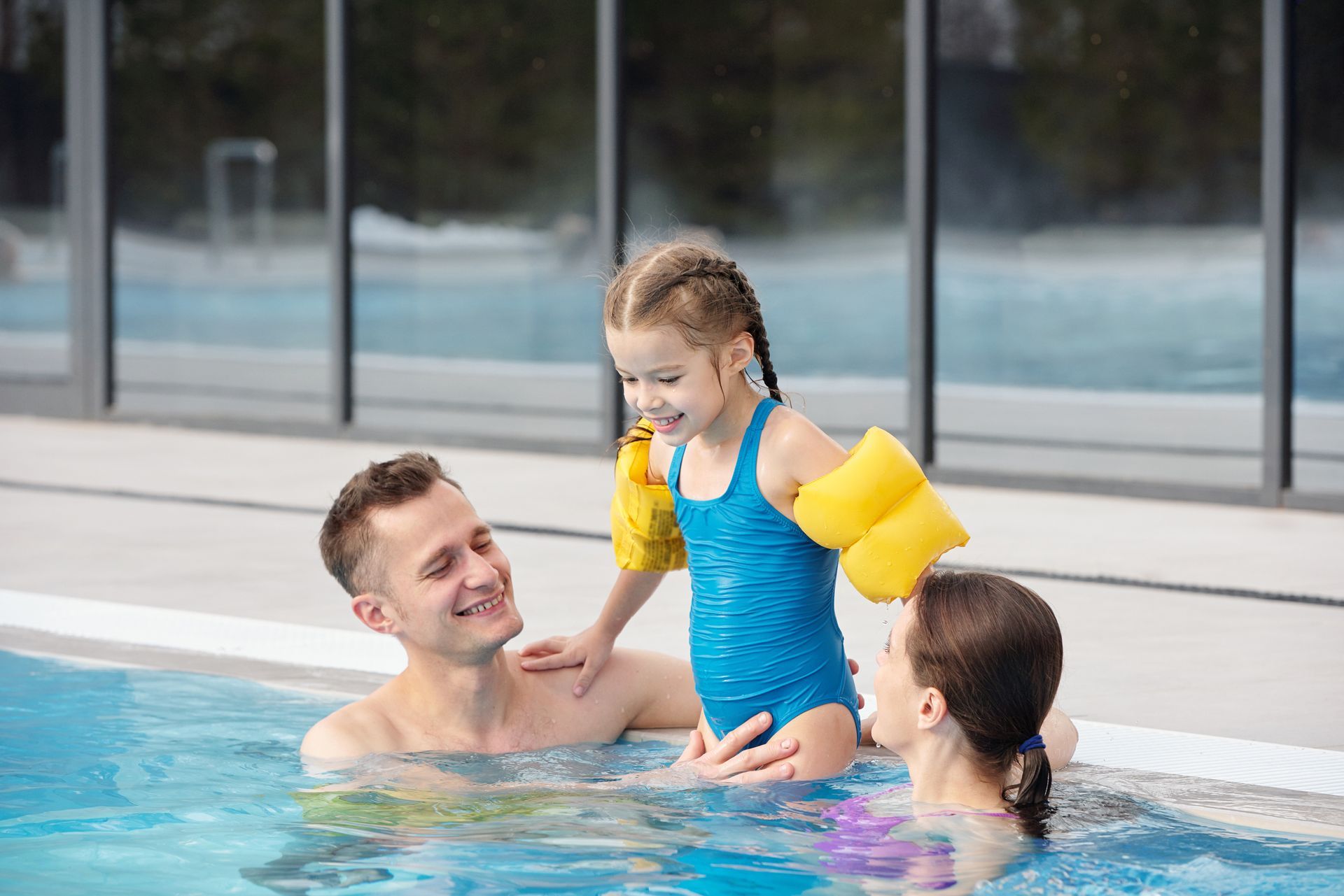 A man , woman and child are playing in a swimming pool.