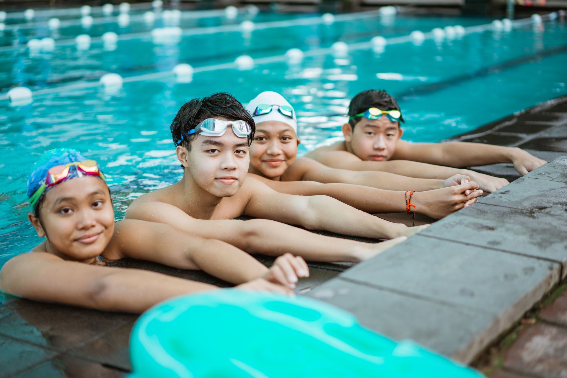 A group of young people are laying on the edge of a swimming pool.