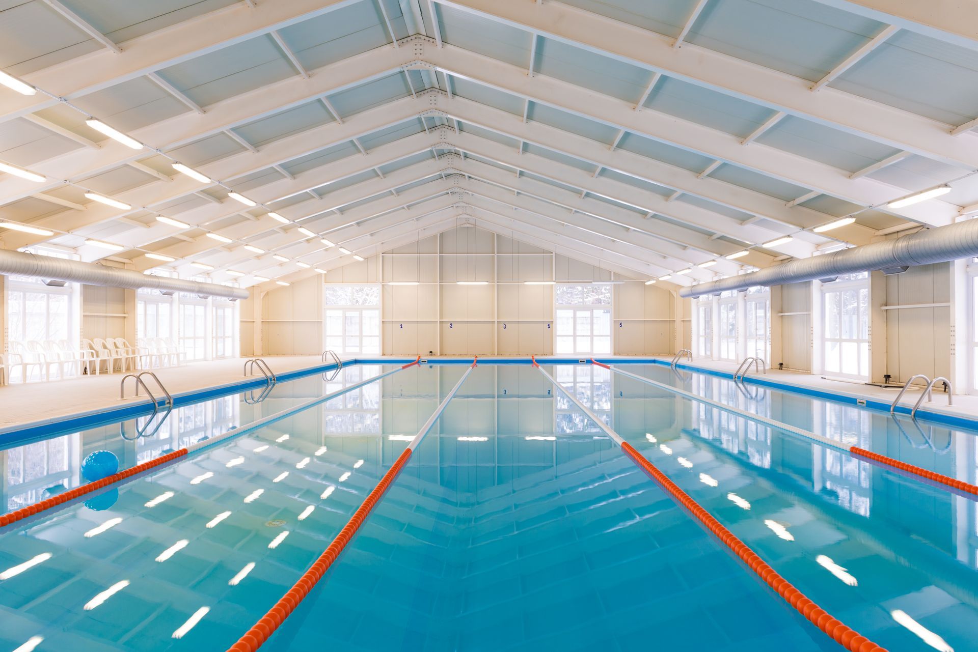 A large indoor swimming pool with a roof and a lot of windows.