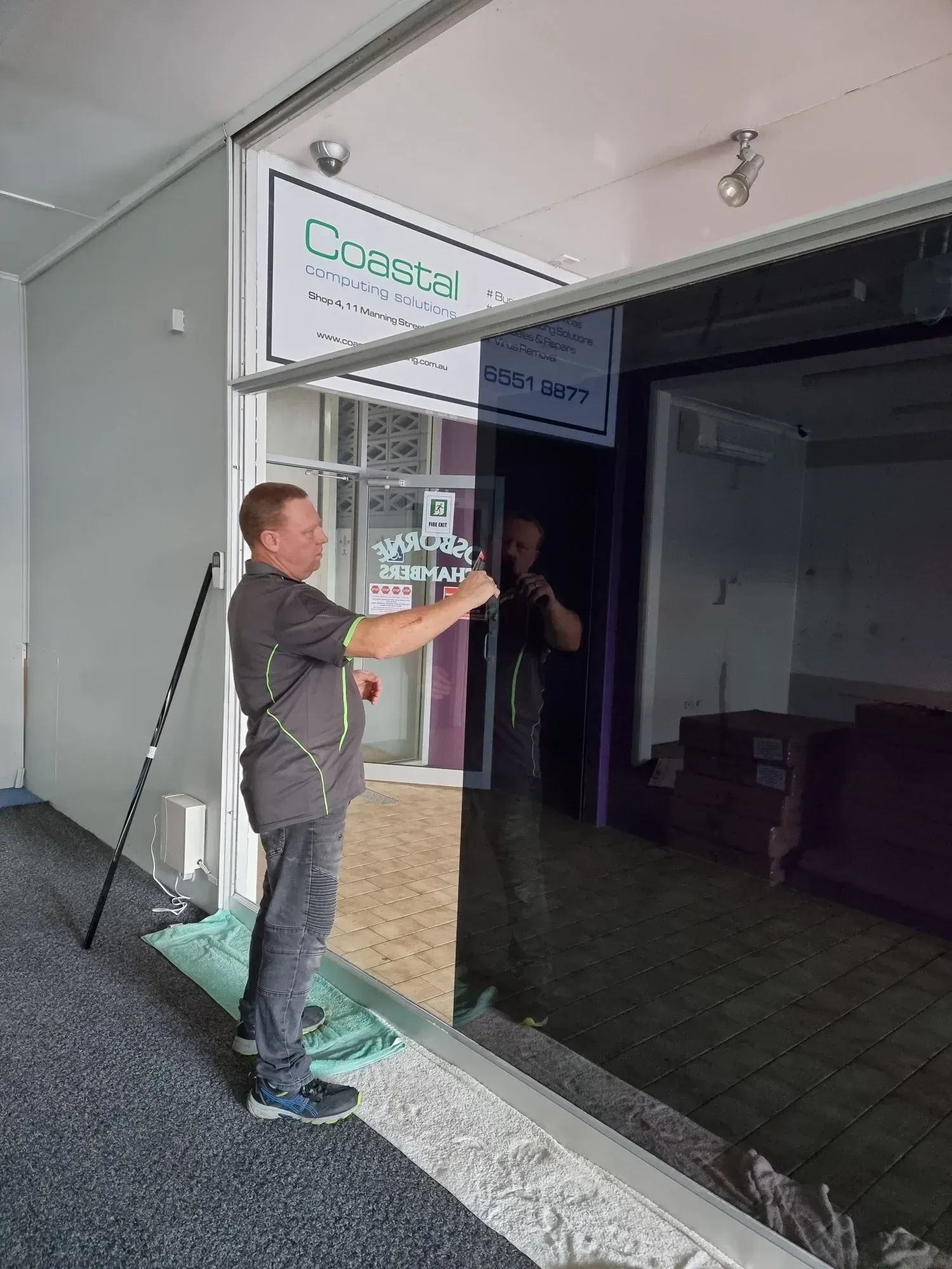 A Man Applying Tint to a Large Glass Window — Awesome Window Tint In Wauchope, NSW