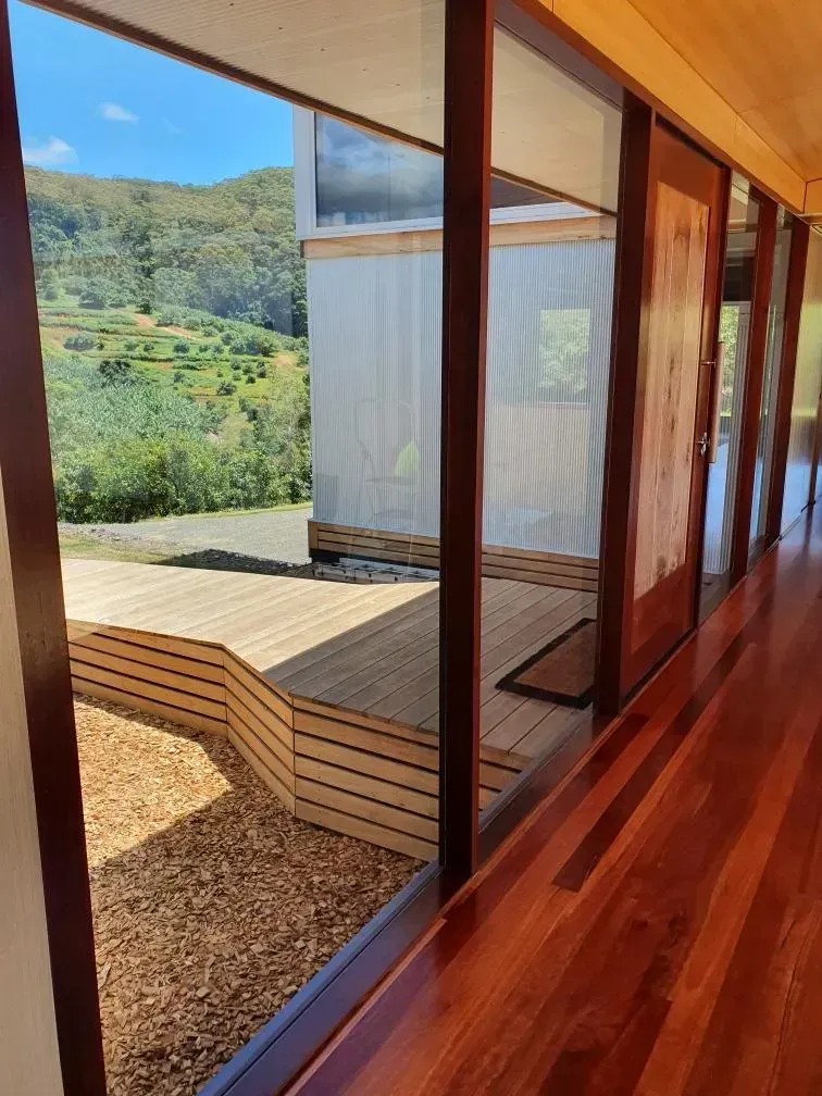 Modern cabin interior with large glass wall overlooking a sunny green hillside and outdoor wooden deck — Awesome Window Tint In Kempsey, NSW