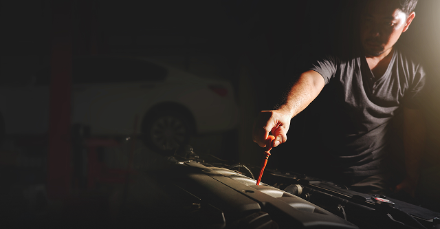 Person holding a dipstick over an engine bay in a dimly lit garage | The Recon Garage