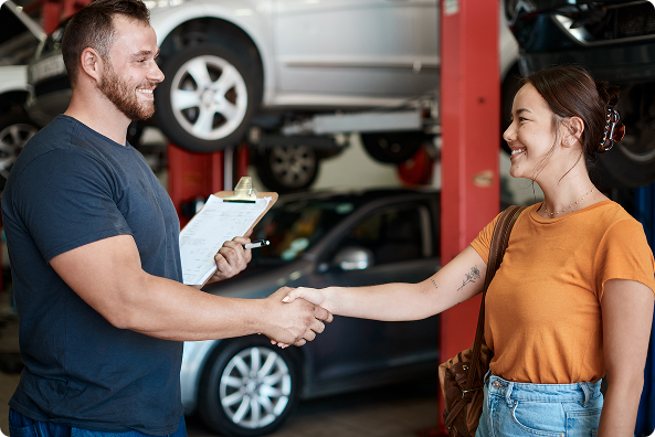 Two people shaking hands in an auto repair shop, with a car lifted in the background. | The Recon Garage