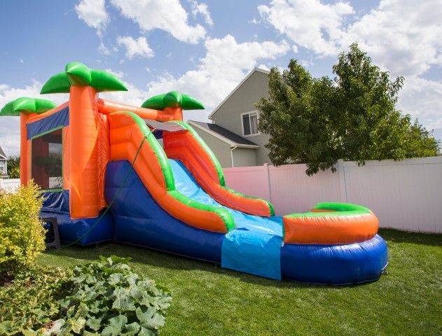 Colorful orange, blue, and green inflatable backyard slide on a grassy lawn beside a house