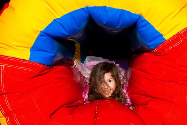 Child peeking out of a colorful red, yellow, and blue inflatable tunnel slide