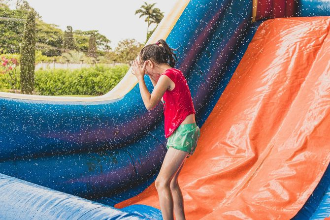Child in red shirt and green shorts climbs a blue and orange inflatable slide outdoors