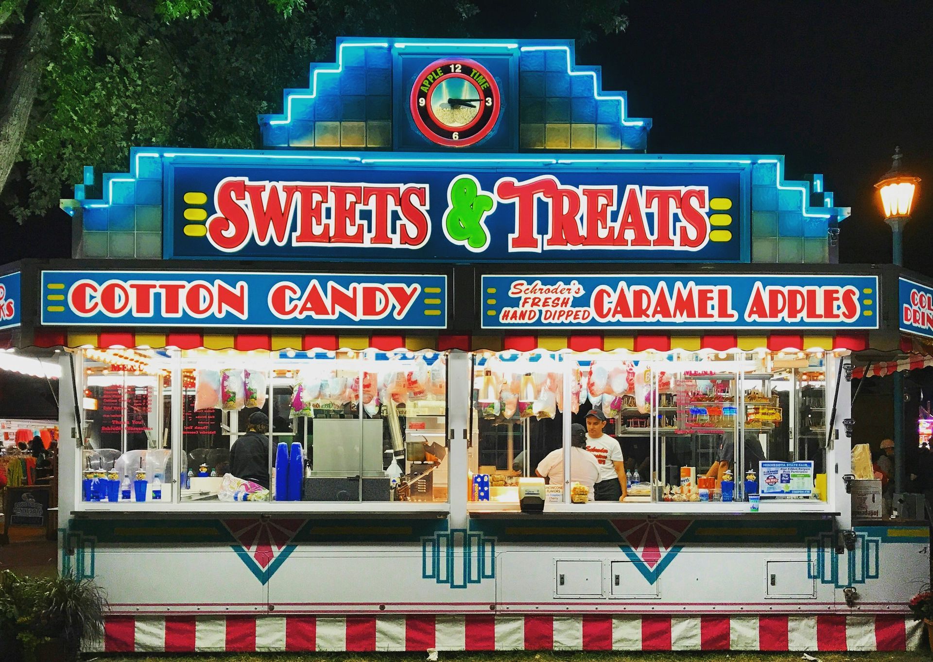 Brightly lit Sweets & Treats stand selling cotton candy and caramel apples at night