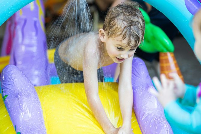 Child playing on a colorful inflatable water slide, splashing through purple, yellow, and blue tubes